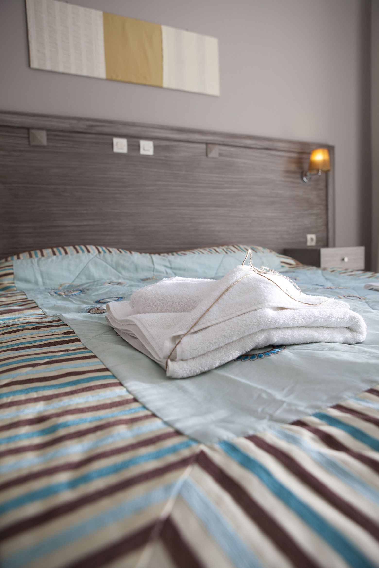 Ein ordentlich gemachtes Bett mit einer gestreiften Tagesdecke und einem gefalteten weißen Handtuch.