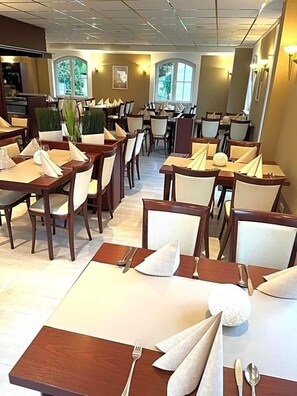A dining area with multiple tables set for service, chairs arranged around each table, and a window providing natural light.