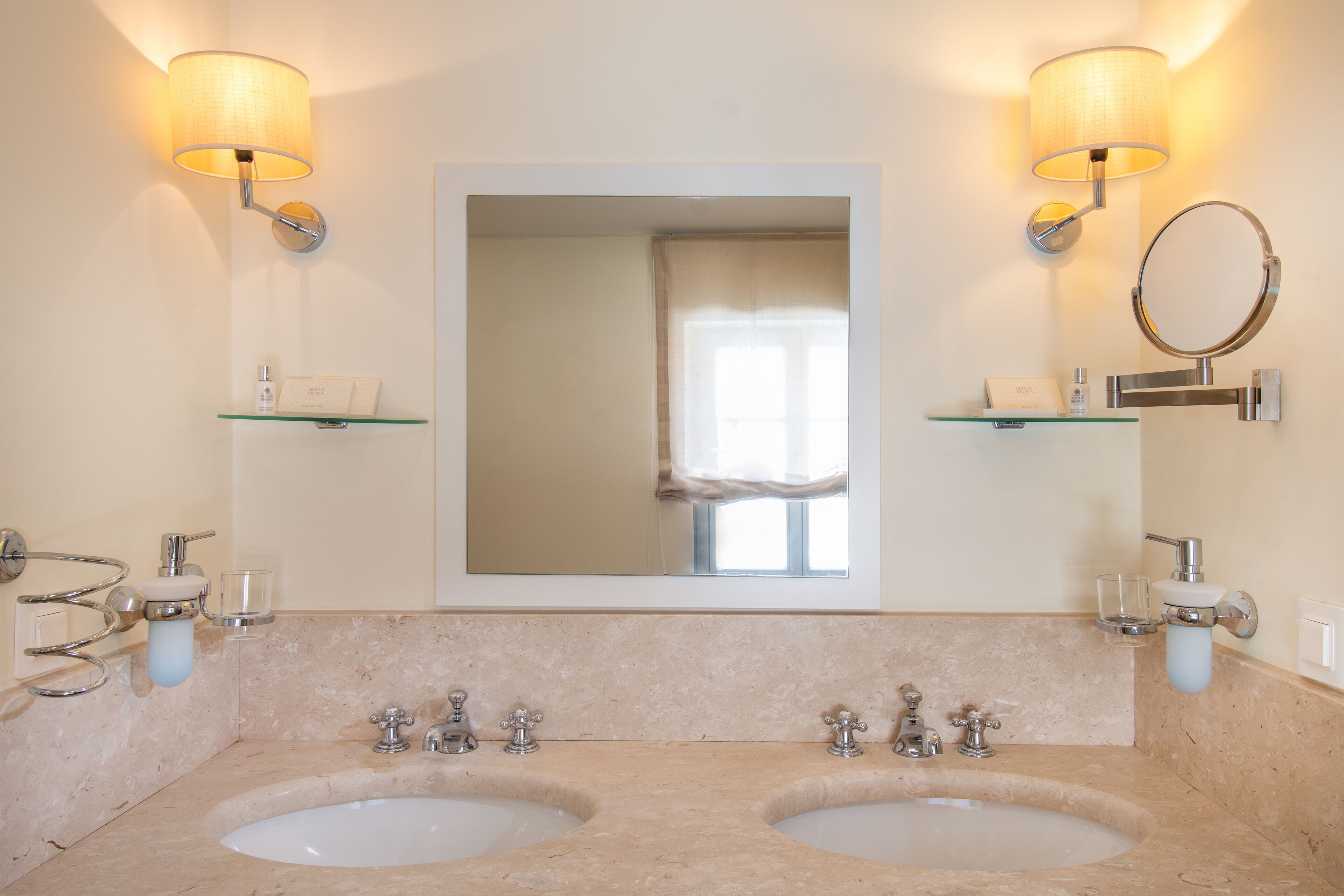 A bathroom with two sinks, a large mirror, and wall-mounted lamps.