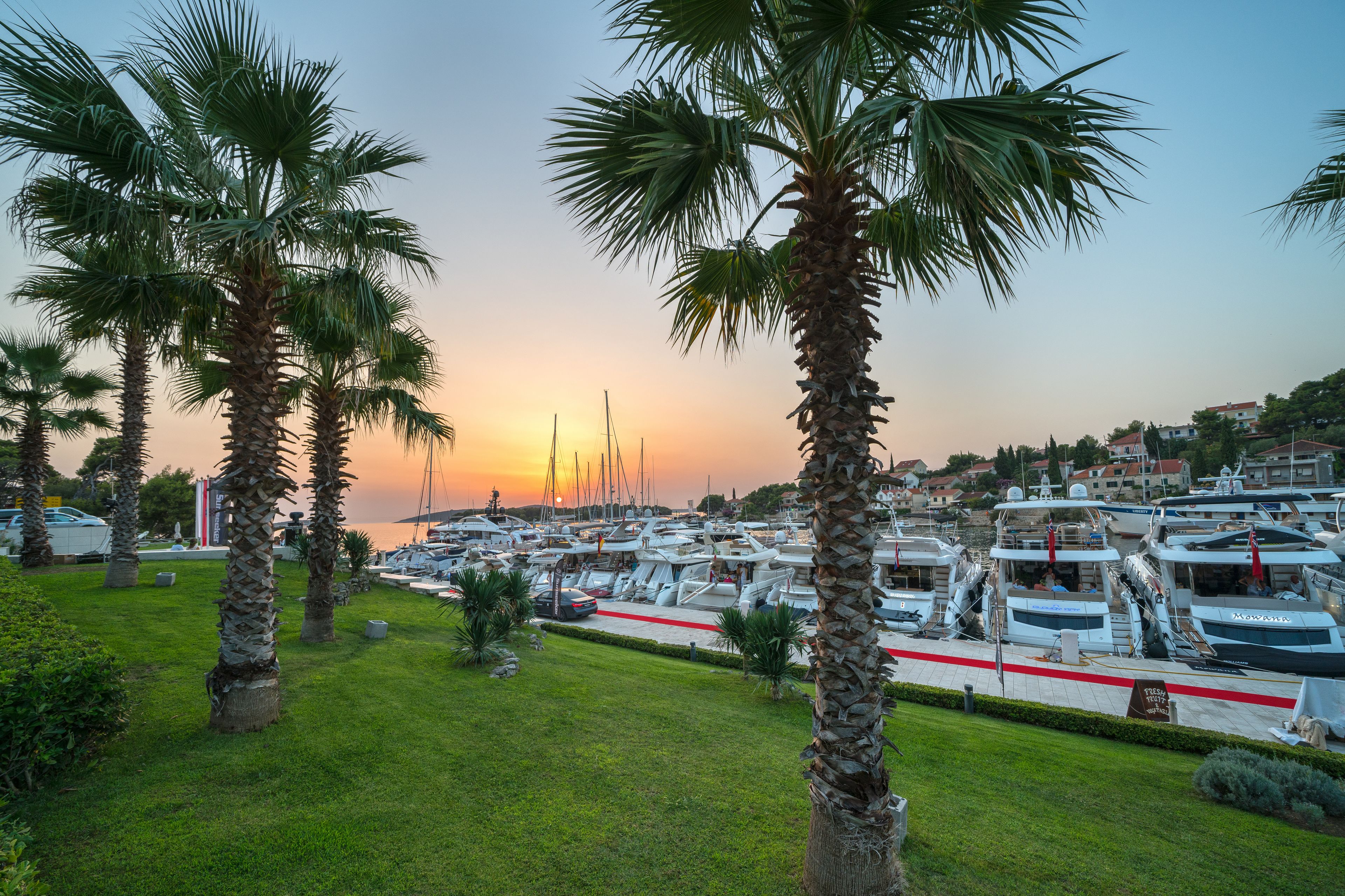 Un port de plaisance avec des bateaux amarrés, entouré de palmiers et un coucher de soleil en arrière-plan.