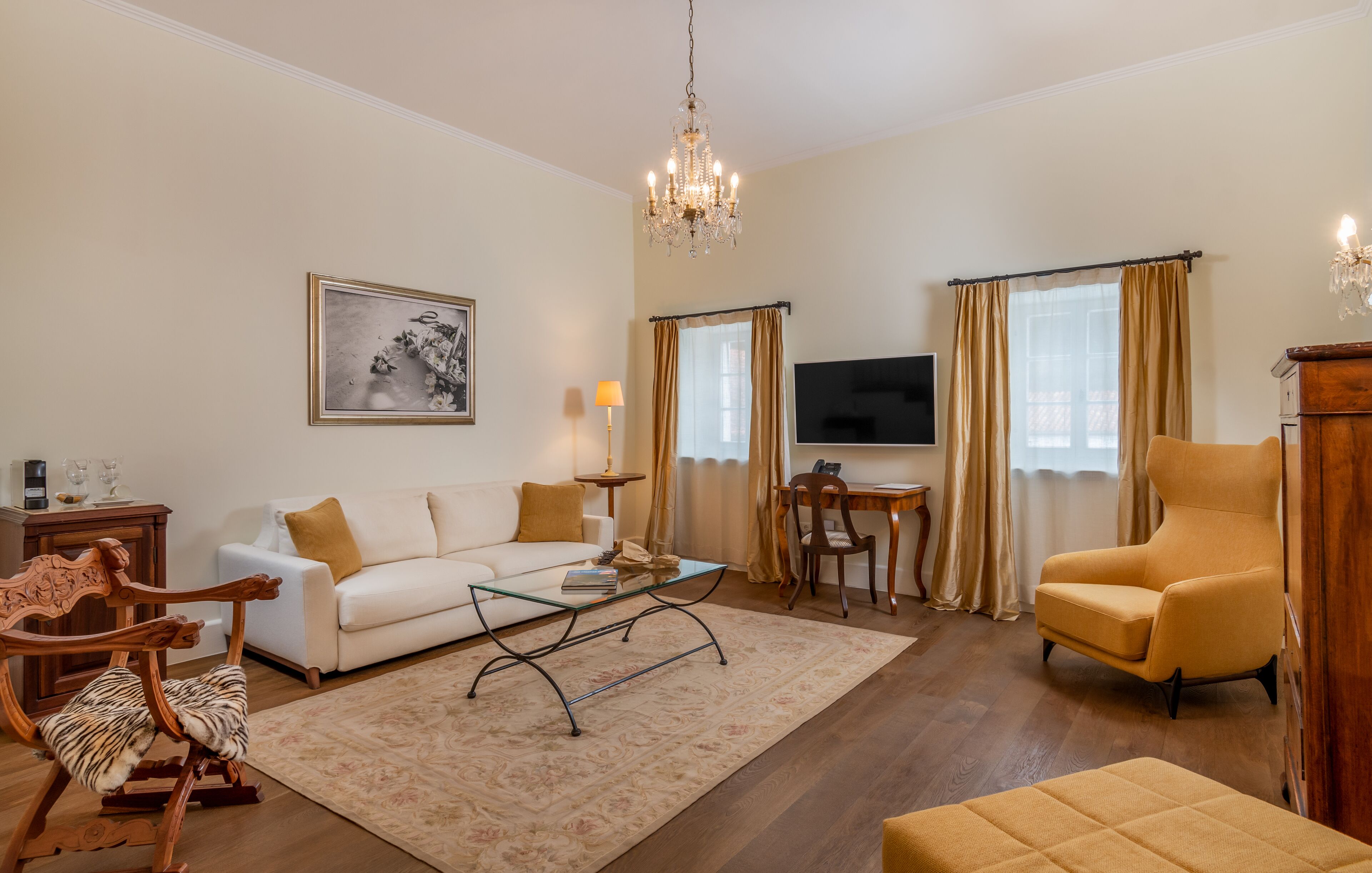 Un salon comprenant un canapé, un fauteuil, une table basse, des chaises en bois, un téléviseur et un lustre.