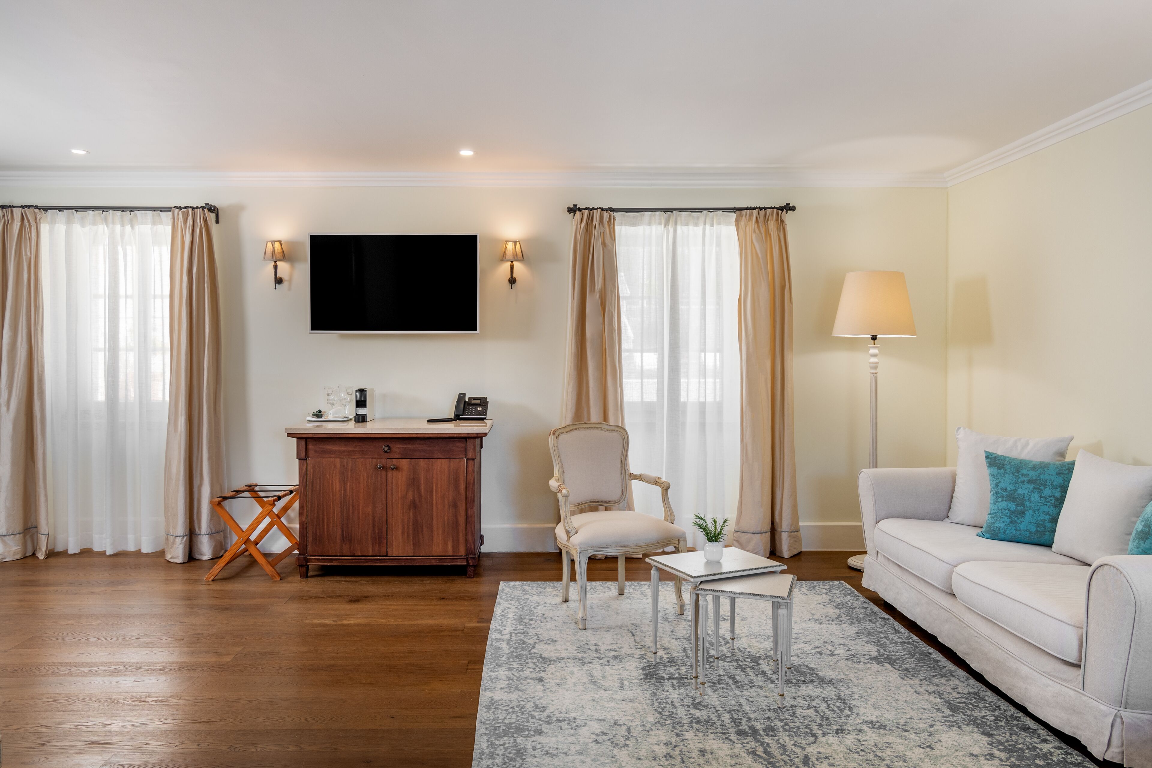 A living room with a wooden floor, a white sofa, a small table, a chair, a TV, and a lamp.