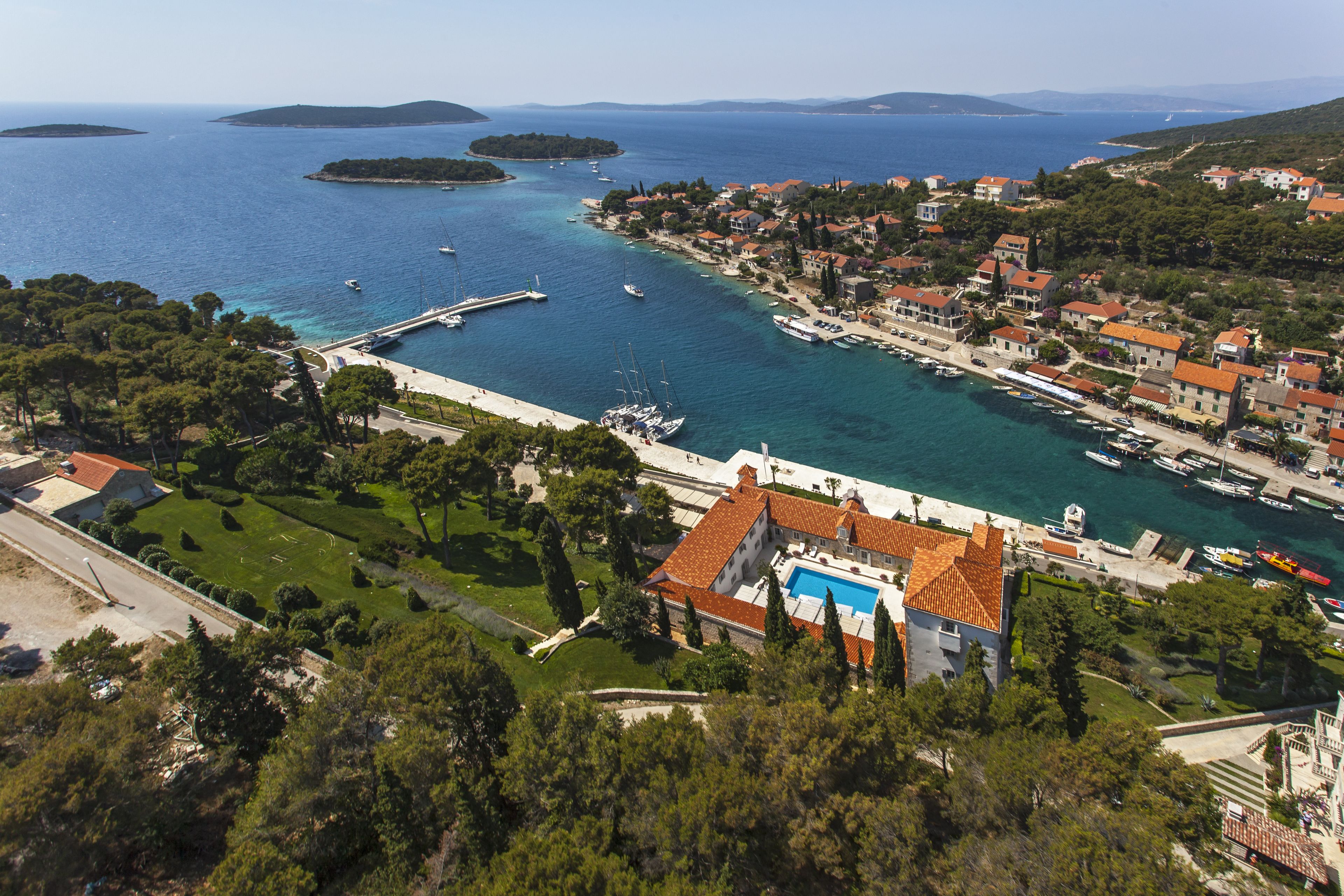 A coastal town with a marina, houses with red roofs, and a large swimming pool.