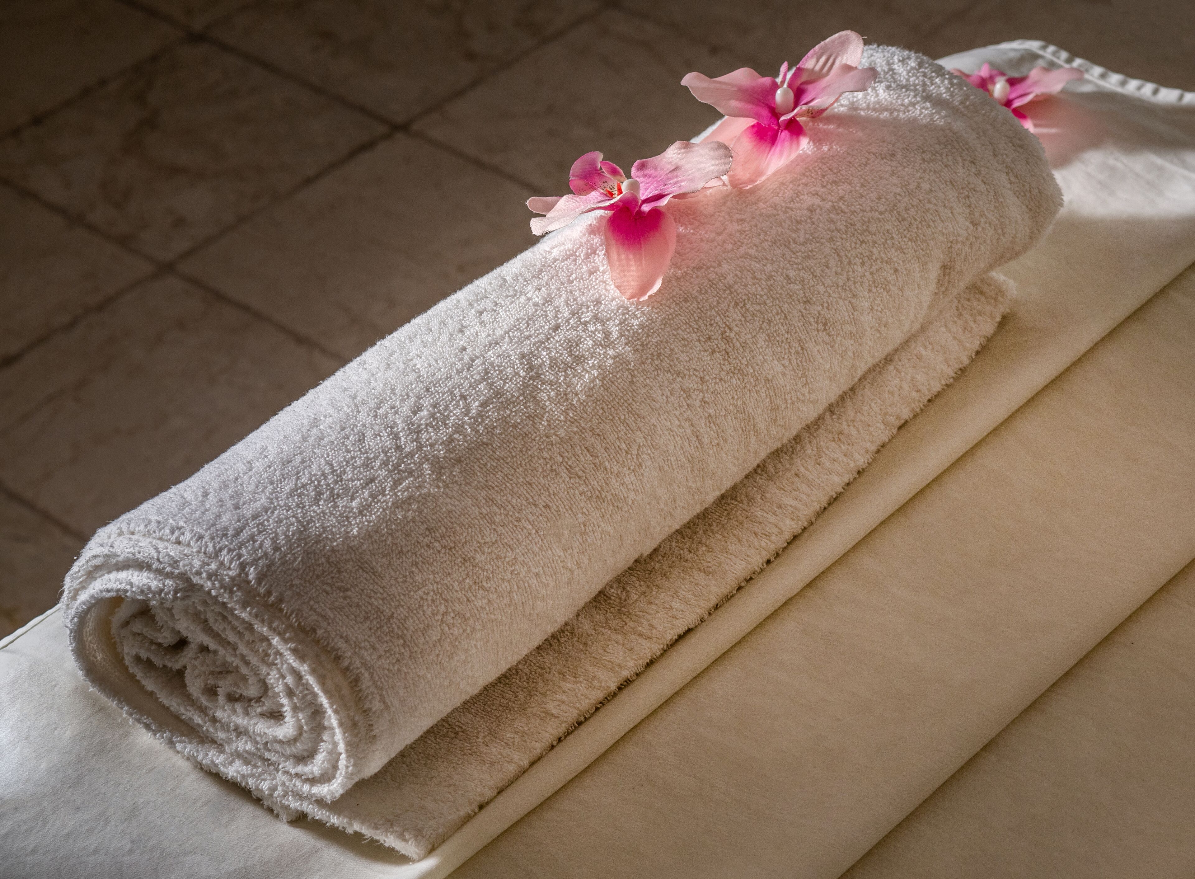 A neatly rolled white towel with pink flowers on a flat surface.