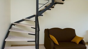 Una scala moderna dal design minimalista, un divano marrone con un cuscino color senape e un pavimento in legno chiaro.