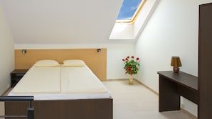 Una camera da letto con un lucernario, un letto, un comodino, una scrivania e un vaso con fiori.
