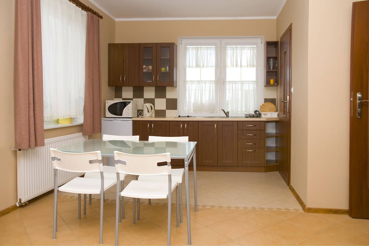 Cocina compacta con una mesa de vidrio, sillas blancas, microondas y armarios de madera.