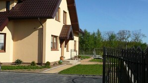 Una casa a due piani con tetto in tegole marroni, un camino e una strada di accesso lastricata che porta a un ingresso chiuso da cancello.