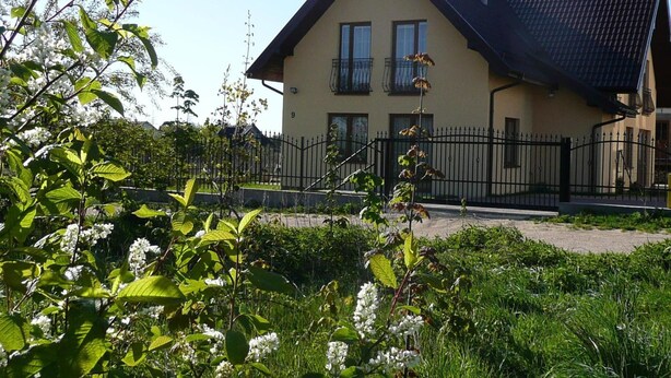 Una casa a due piani con tetto scuro, un balcone al secondo piano e un cancello in metallo nero davanti.