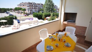 A balcony with a table set for breakfast, chairs, and a view of a parking lot and buildings. - Residence Cleo (Comacchio)