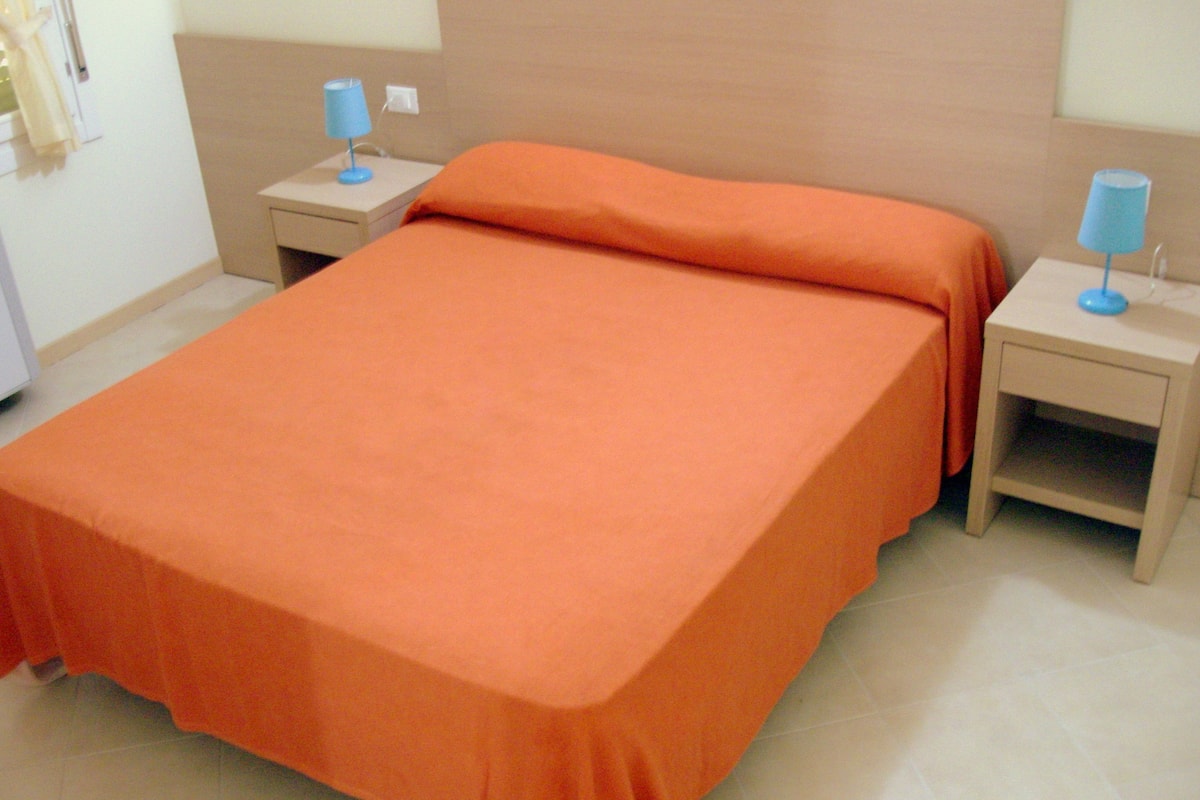 A standard hotel room with a single bed, two bedside tables with lamps, and a plain wall.
