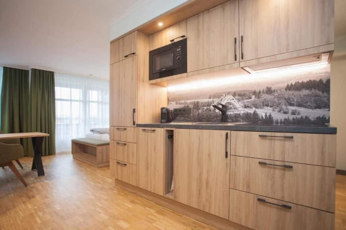 A modern kitchen with wooden cabinets, a microwave, and a built-in oven. There is a dining area with a table and chairs.