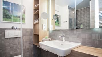 A modern bathroom with a large mirror, a white sink, and a shower area.
