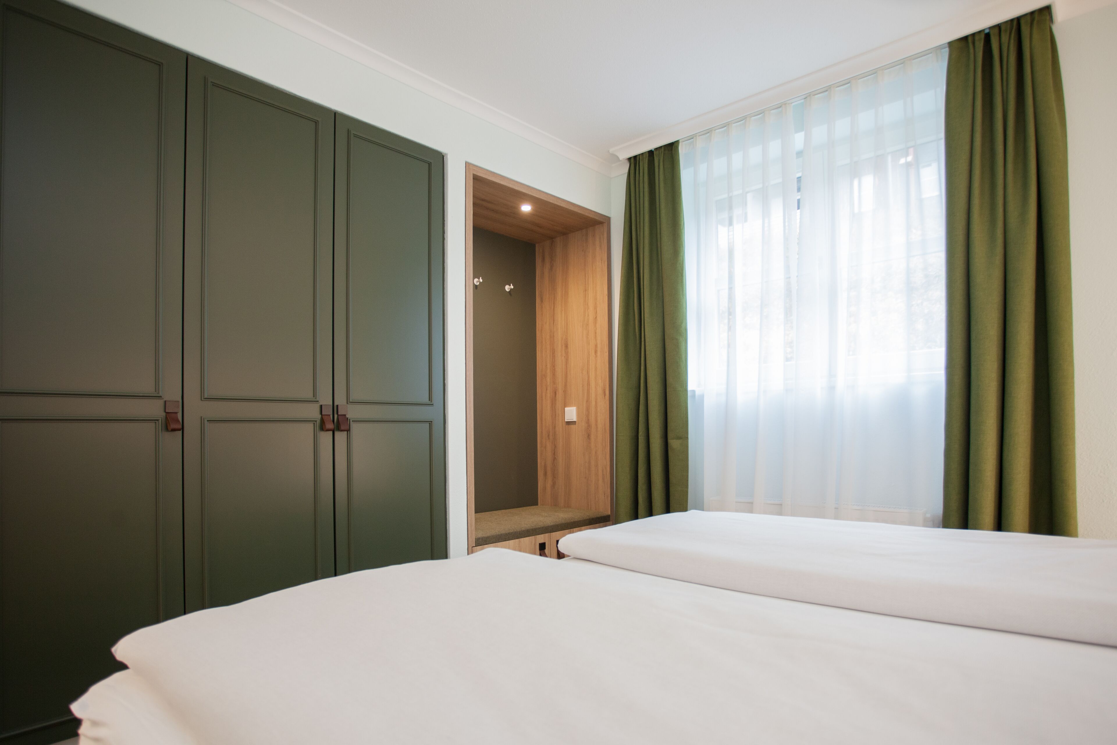 A hotel room with a large wardrobe, a built-in bench, and a bed.