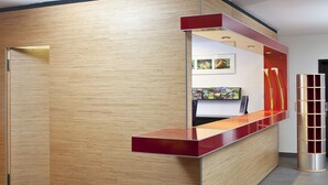 A reception desk with a wooden panel backdrop and a red counter. - Hapimag Resort Winterberg (Winterberg)