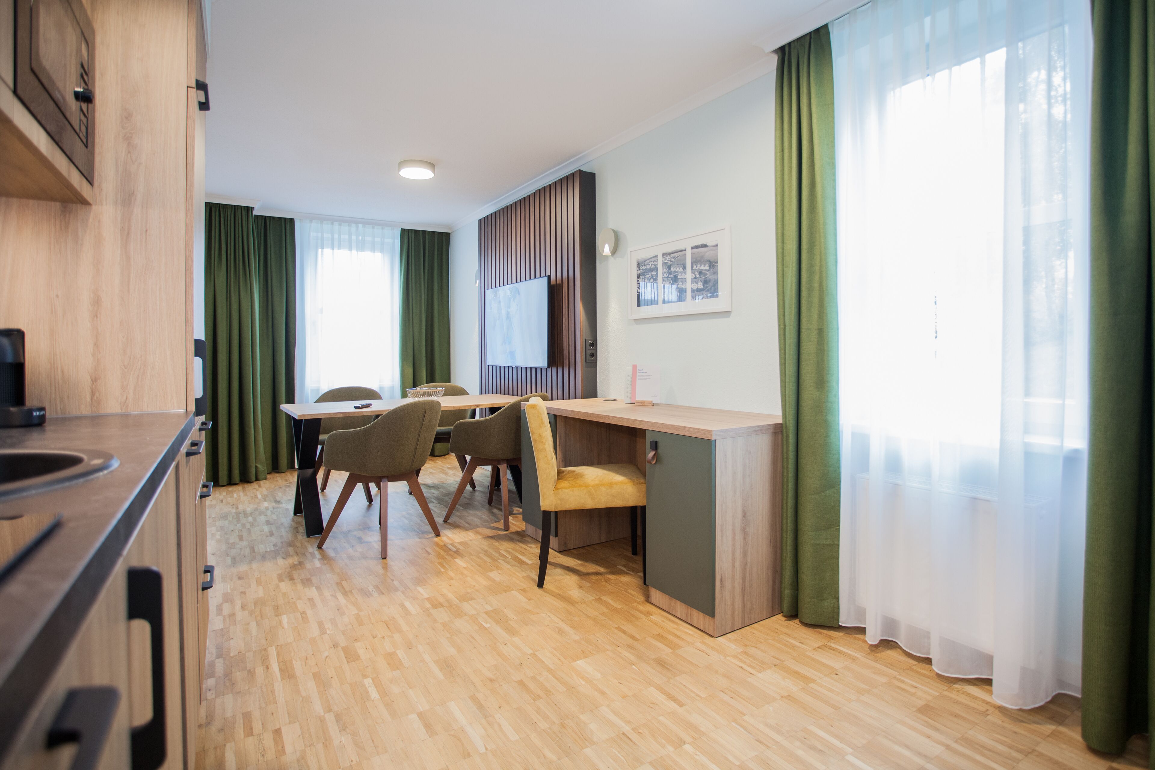Eine moderne Küche mit Holzausbau, ein Essbereich mit Tisch und Stühlen sowie ein großes Fenster mit grünen Vorhängen.