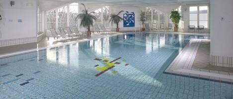 An indoor swimming pool with clear water, tiled floor, and several lounge chairs.