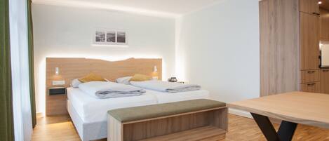 A modern hotel room with a neatly made bed, a wooden headboard, a bedside table with a lamp, and a small window.