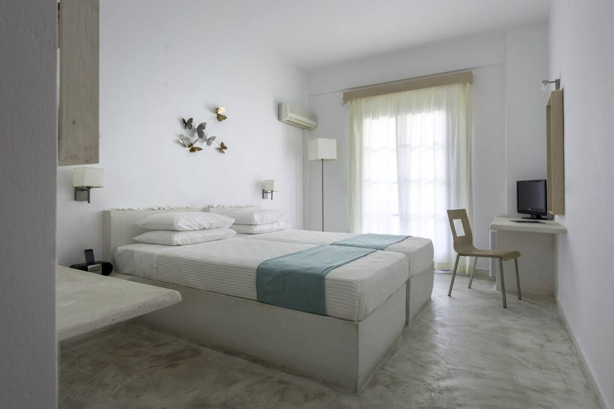 Un dormitorio minimalista con una cama grande, un escritorio con una computadora y una silla.