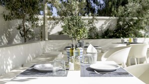 An outdoor dining area with white tables, olive branches, and clear glassware. - Hotel 28 (Santorini)