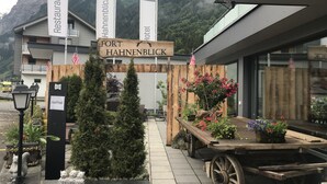 A hotel entrance with a wooden sign, American flags, and a cart with potted plants.