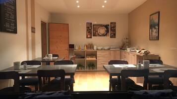 A dining area with tables and chairs, a kitchen area with cabinets and appliances, and a door leading to another room.