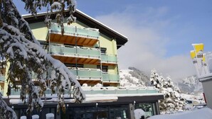 A multi-story building with balconies, surrounded by snow-covered trees and mountains.