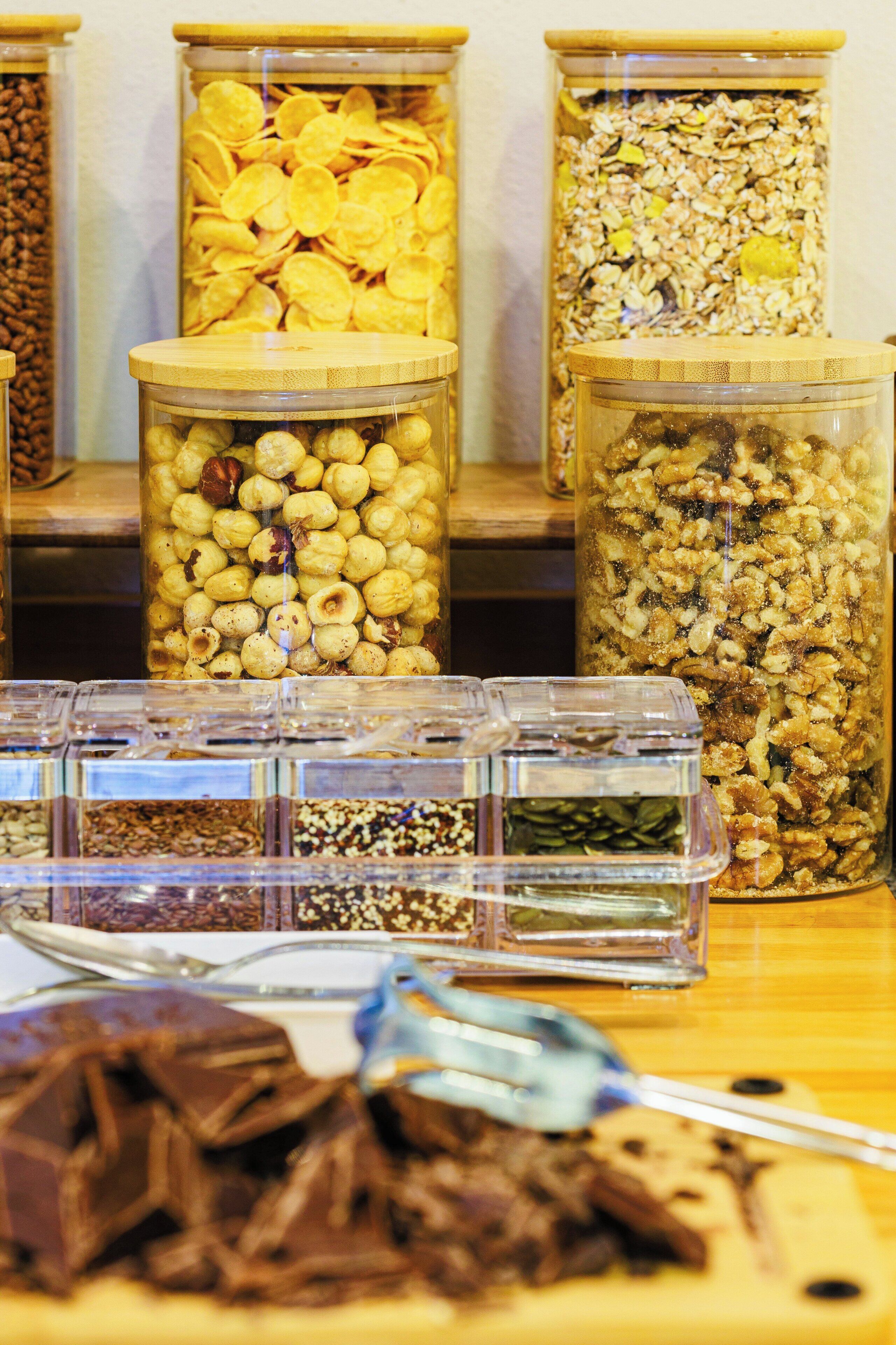 Verschiedene Lebensmittel in Behältern, darunter Nüsse, Samen und Granola.