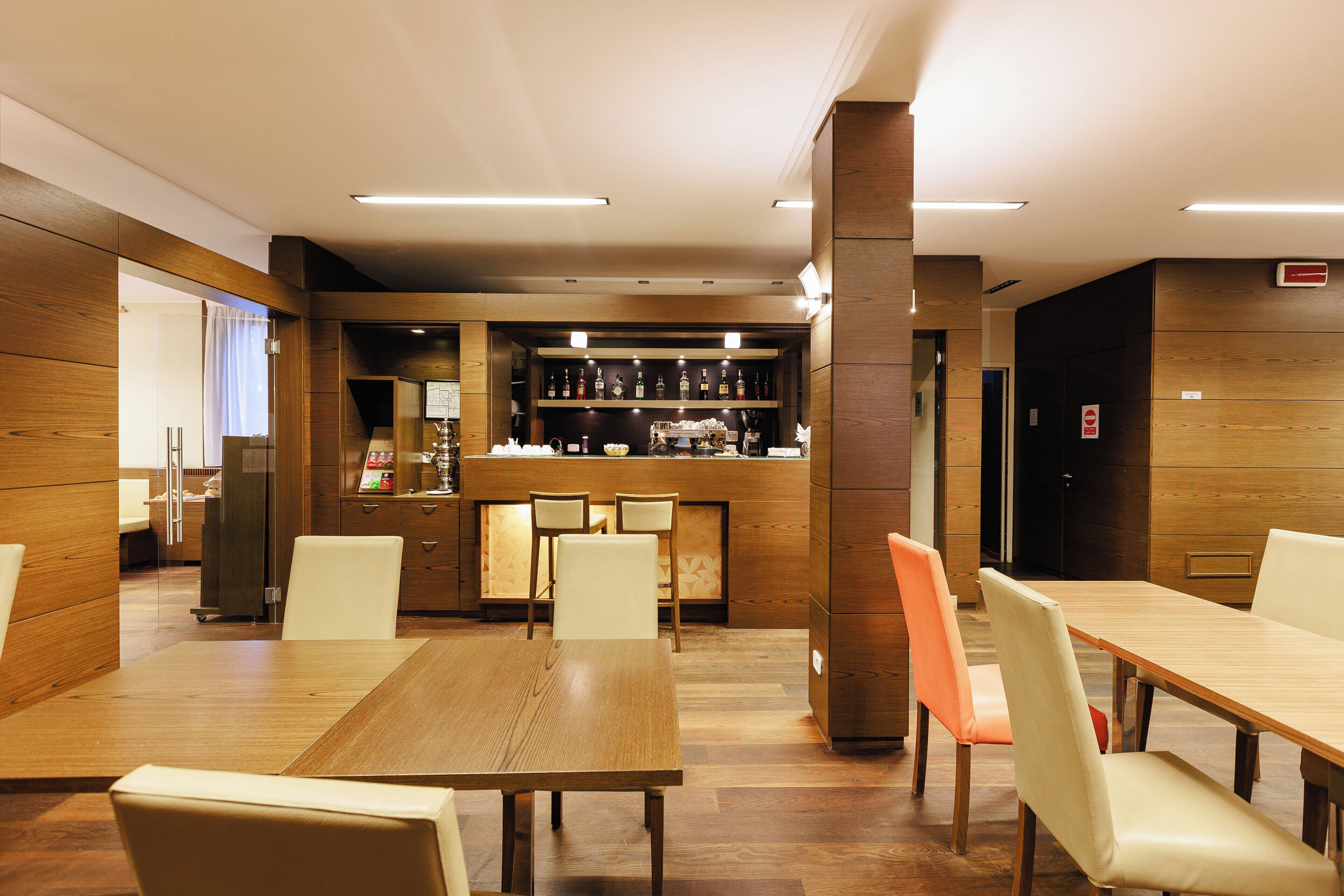 A modern restaurant with wooden paneling, a bar area, and multiple seating options.