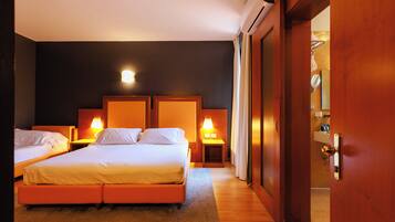 Habitación de hotel con dos camas, suelo de madera y baño visible a través de una puerta abierta.