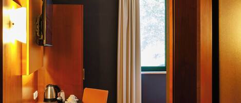 Habitación de hotel con escritorio de madera, una silla, una cama, ventana con cortinas y una puerta.
