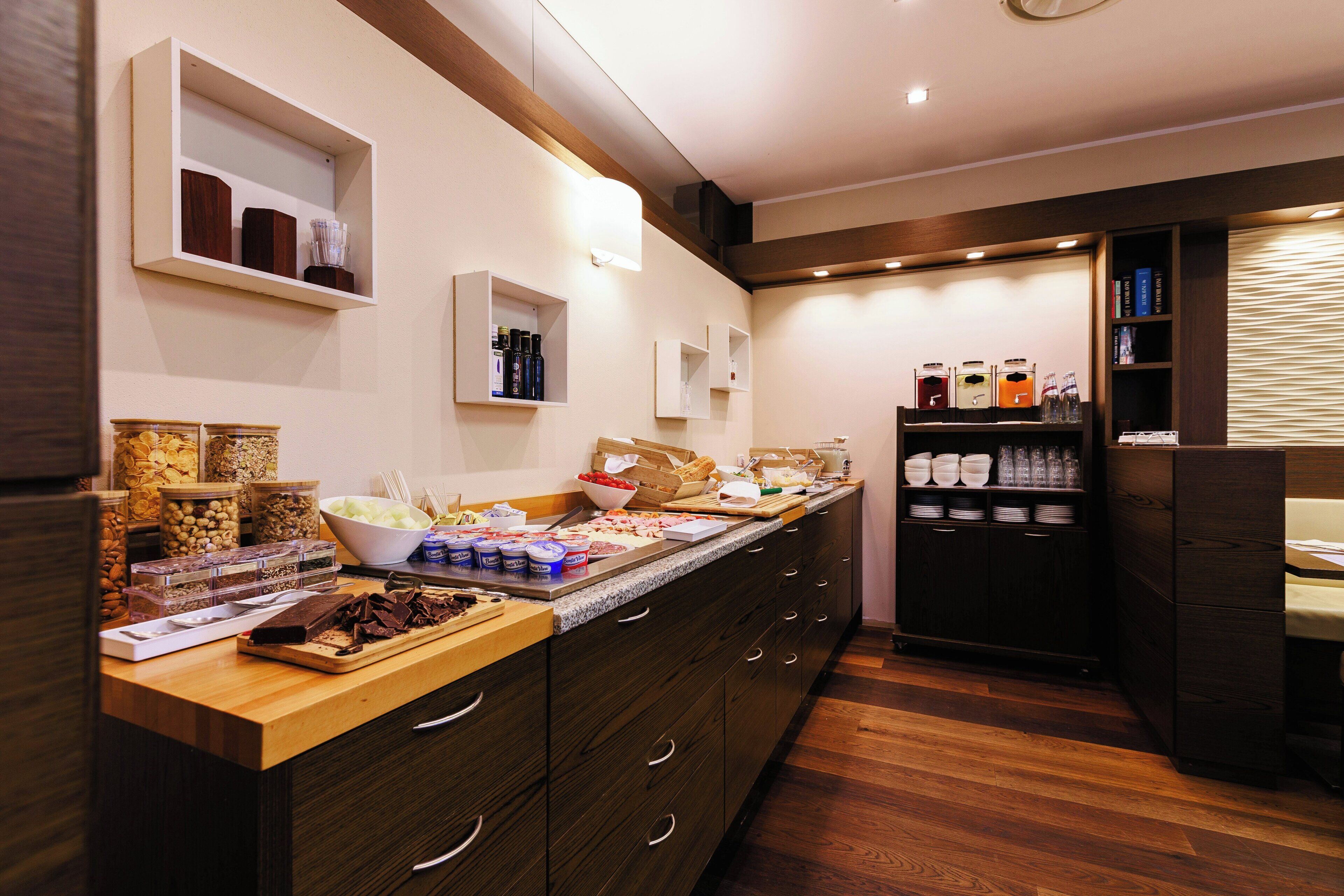 A kitchen area with a long counter, wooden cabinets, and various food items and kitchenware.