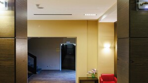 A hallway with wooden paneling, a red chair, a small table with a vase, and a door at the end.