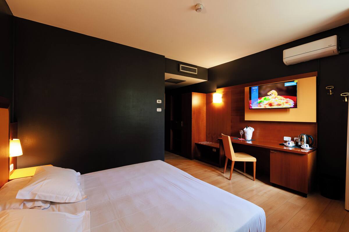 Een hotelkamer met een bed, een bureau, een stoel en een televisie aan de muur.