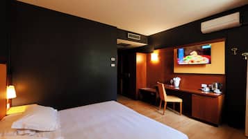 Quarto de hotel com cama, escrivaninha, cadeira e televisão na parede.