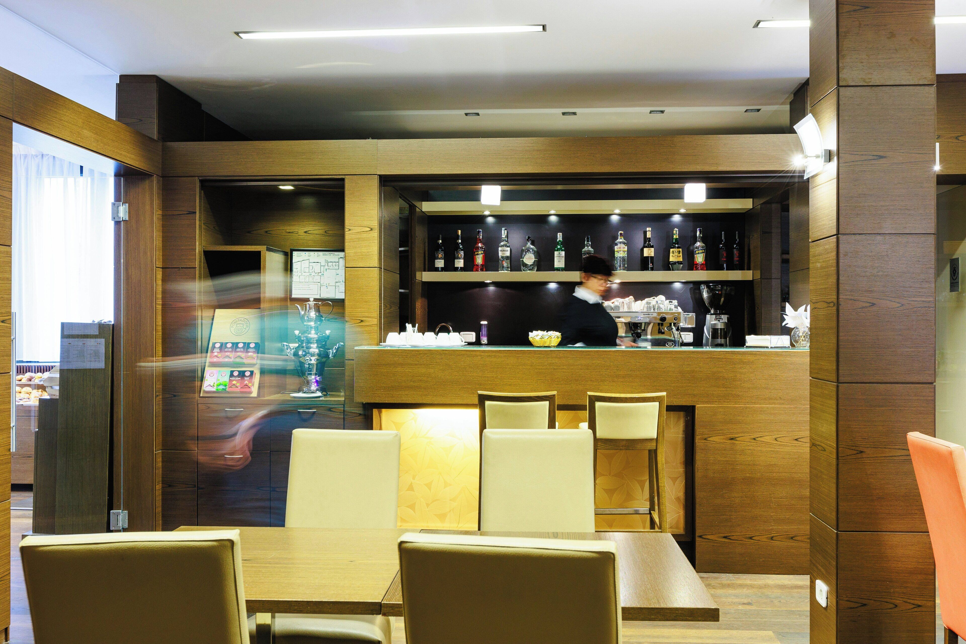 Interior de restaurante com painéis de madeira, área de bar com garrafas e disposição de mesas e cadeiras.