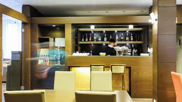 Interior de restaurante com painéis de madeira, área de bar com garrafas e disposição de mesas e cadeiras.