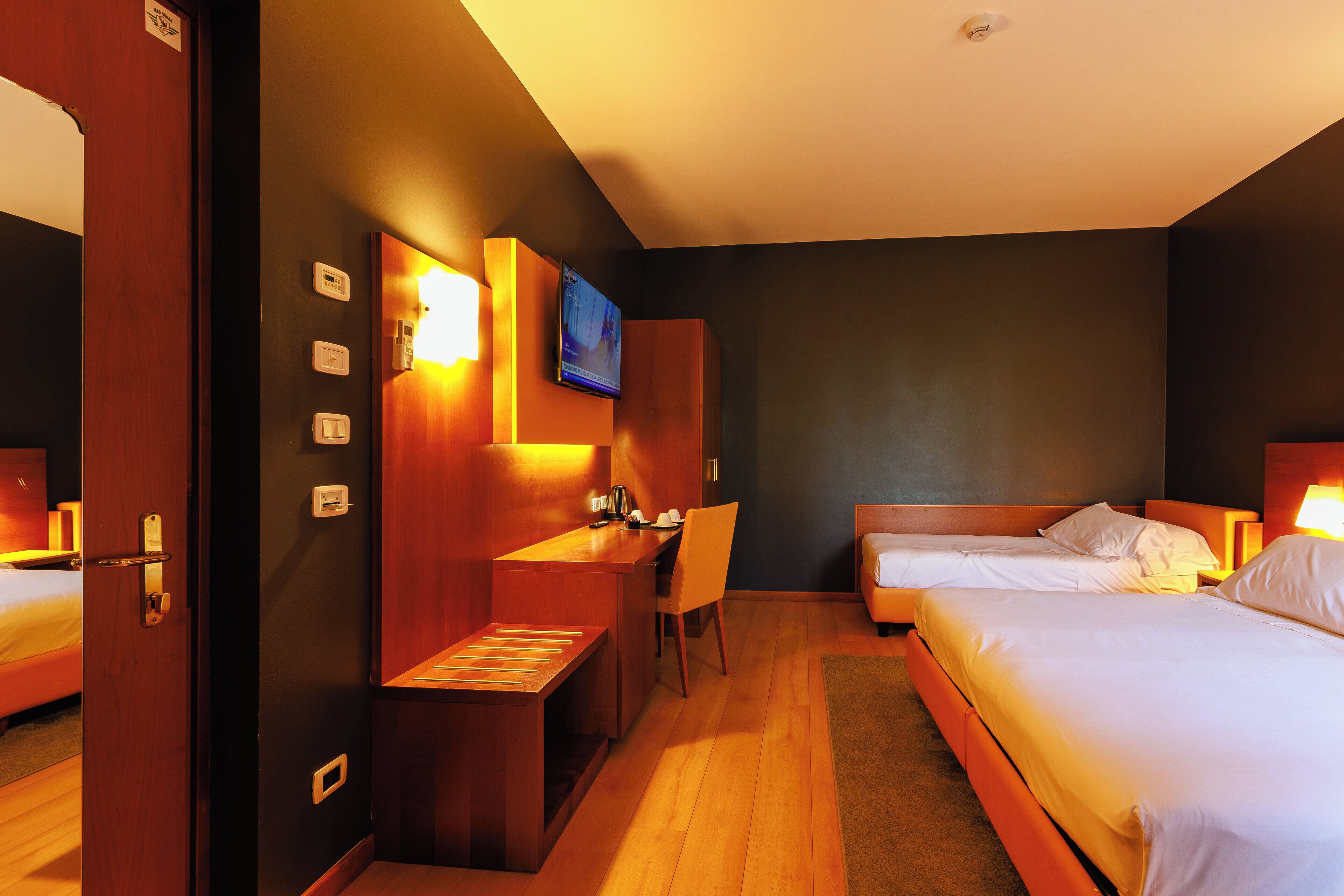A hotel room with two beds, a desk with a chair, a television mounted on the wall, and a small seating area.
