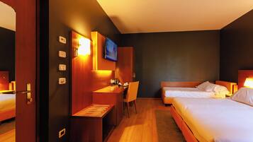A hotel room with two beds, a desk with a chair, a television mounted on the wall, and a small seating area.