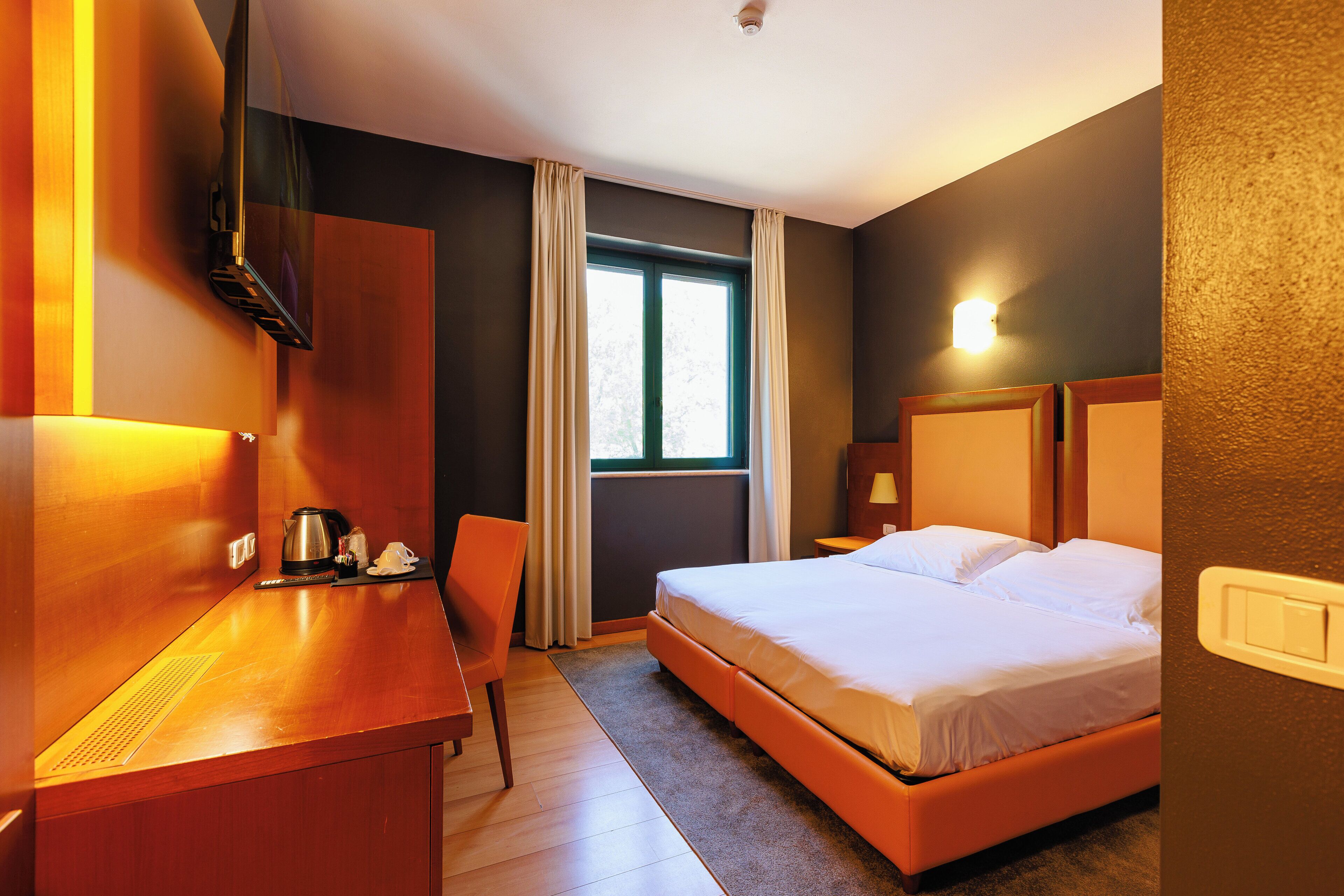 A hotel room with a bed, a desk, a chair, a window, and a television.