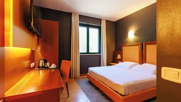 A hotel room with a bed, a desk, a chair, a window, and a television.