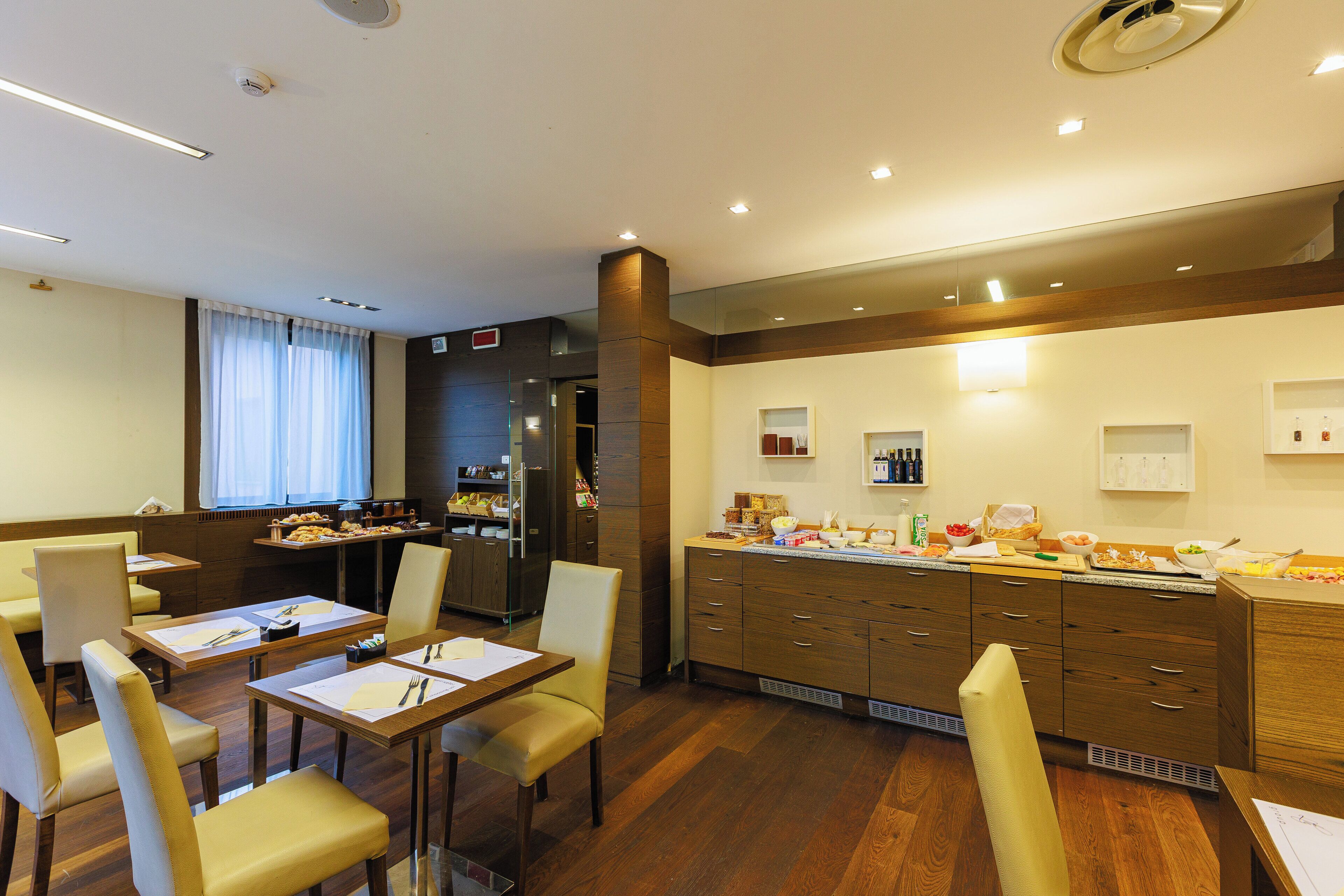 A hotel room with a dining area, a kitchen, and a large window with curtains.