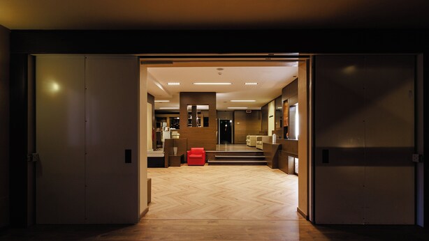 A hotel lobby with a wooden herringbone floor, a red chair, and a staircase leading to the upper floor.