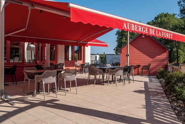 Un espace café en plein air avec des auvents rouges et des meubles en osier.