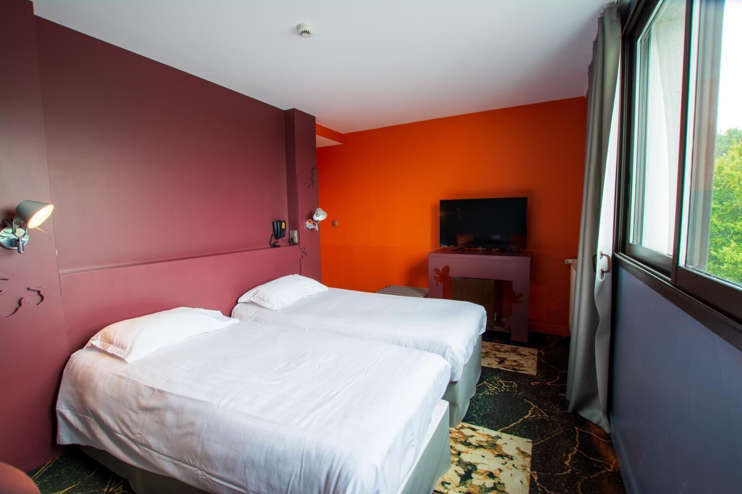 Une chambre d’hôtel avec deux lits, une télévision, un bureau et une fenêtre donnant sur un paysage agréable.