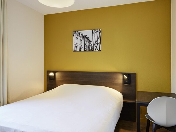 Habitación de hotel con una cama, una mesa y una silla. Hay un cuadro en la pared sobre la cama.