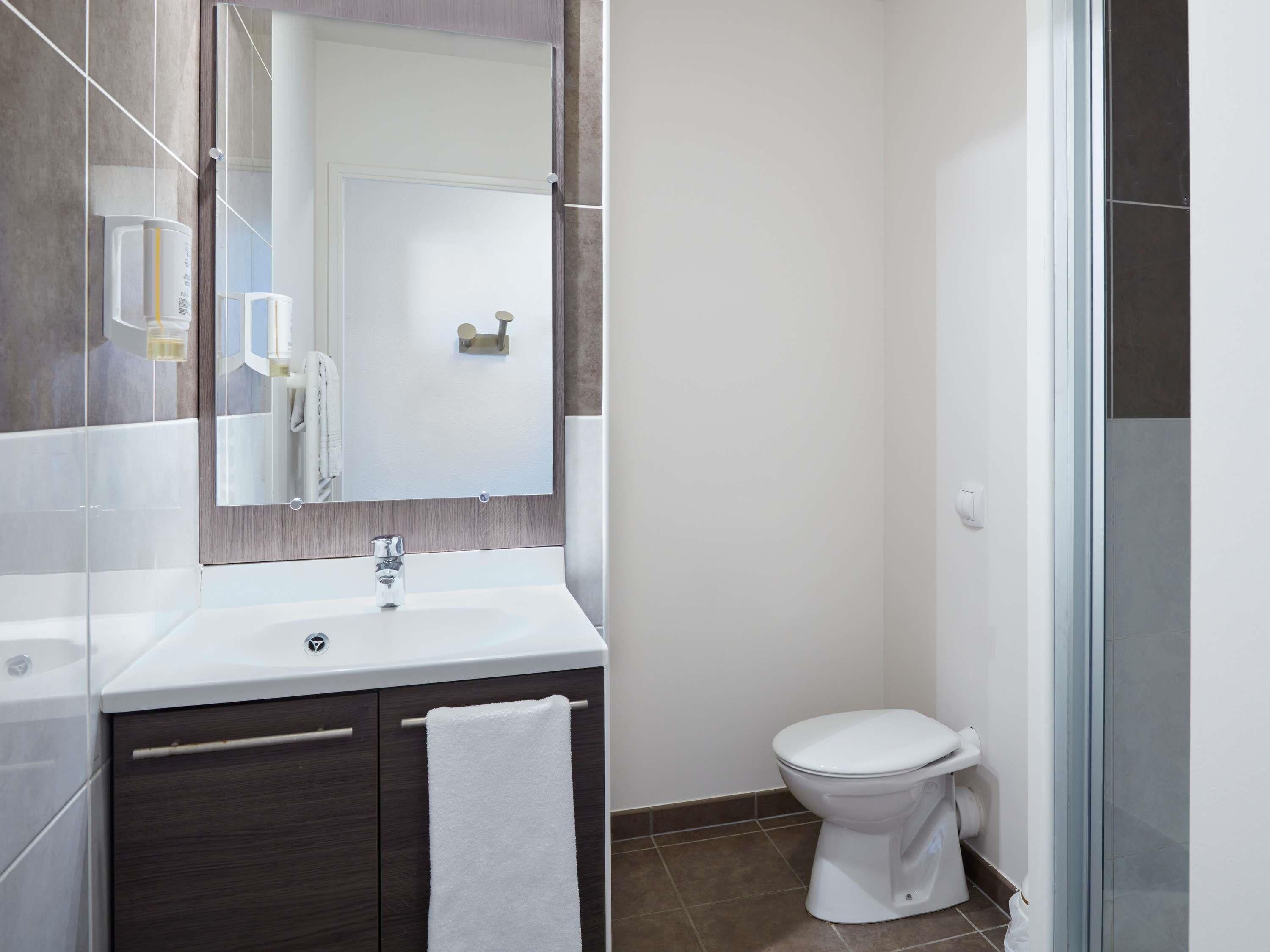 A modern bathroom with a white sink, dark wooden vanity, a glass shower enclosure, and a white toilet.