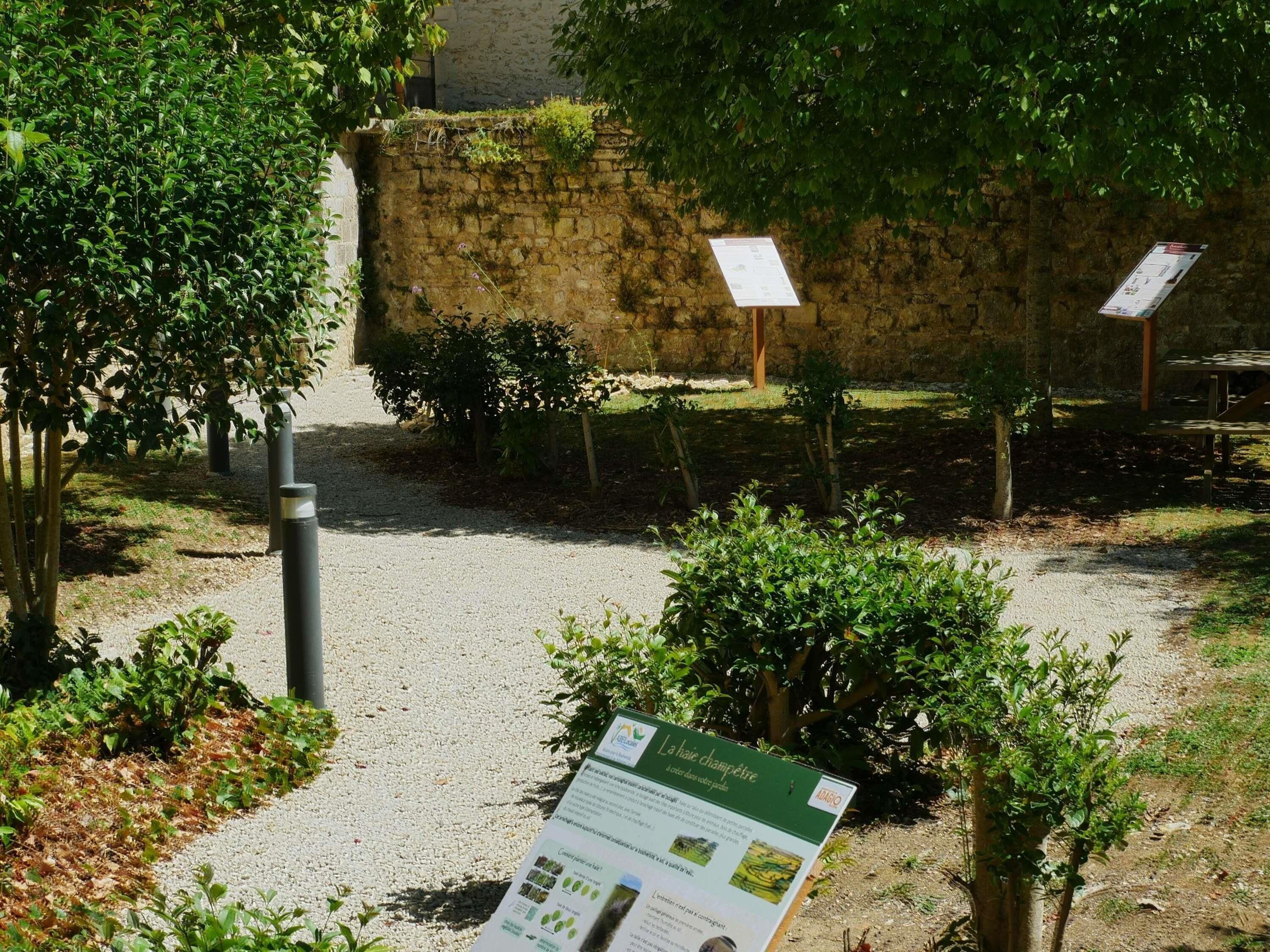 Un espace jardin agrémenté d’un chemin de gravier, d’un mur en pierre et de panneaux d’information.