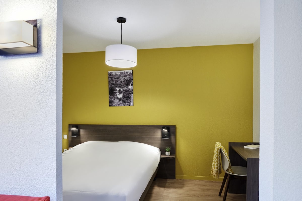 Ein Hotelzimmer mit Bett, Nachttisch, Lampe, Sessel und einem Bild an der Wand.