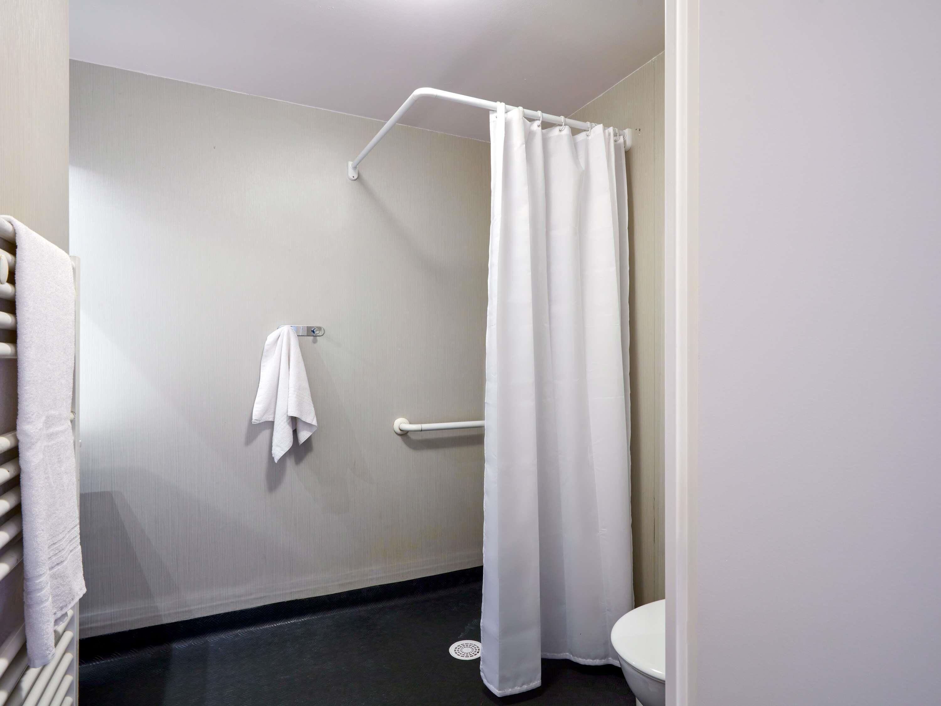 A bathroom with a white shower curtain, a white towel hanging on a towel rack, and a white toilet.